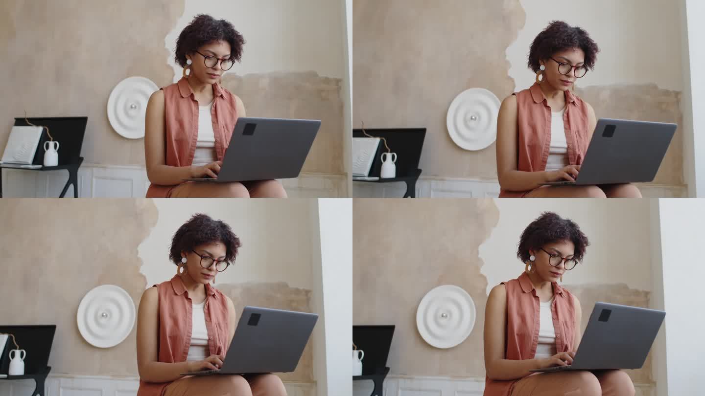 戴眼镜的混血年轻女子在时髦的客厅里用笔记本电脑打字