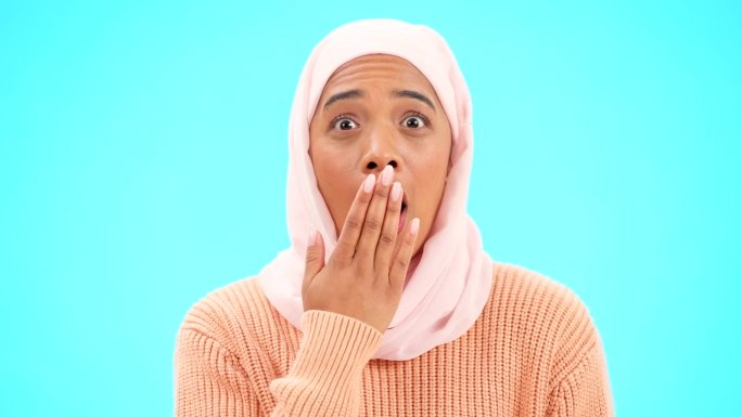 穆斯林妇女，用手捂着嘴拍模特、广告或促销。一名伊斯兰女性戴着头巾，在蓝色背景上用表情符号表达对销售、