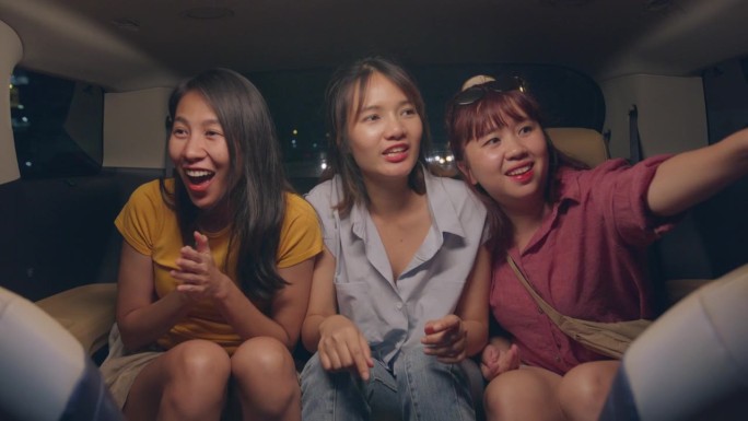 一群年轻的亚洲朋友在晚上开着车在城市里兜风去度假。汽车旅游目的地。