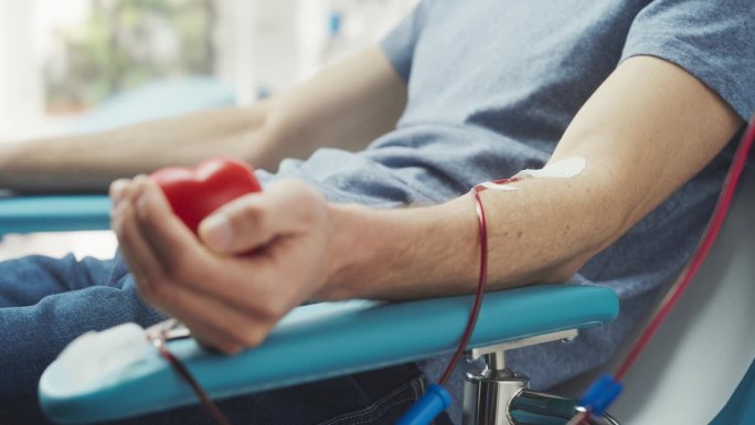 男性献血者的手与附置导管的特写镜头。男性挤压心形红球，将血液通过管道泵入袋中。需要输血的病人的捐献。