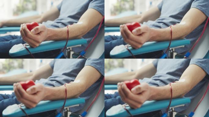 男性献血者的手与附置导管的特写镜头。男性挤压心形红球，将血液通过管道泵入袋中。需要输血的病人的捐献。