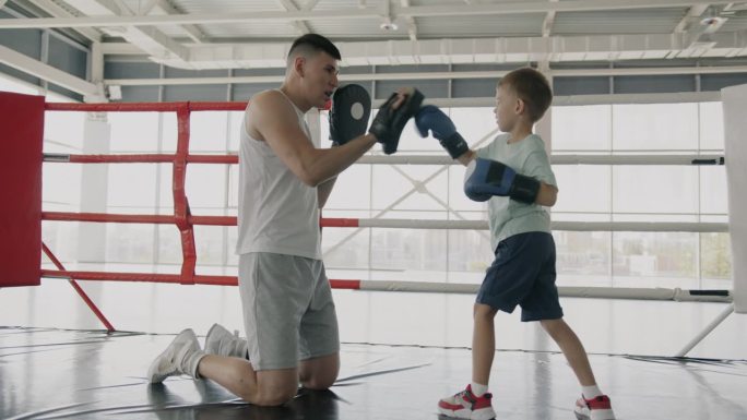慈爱的父亲职业拳击手教儿子武术与孩子解释动作在健身房