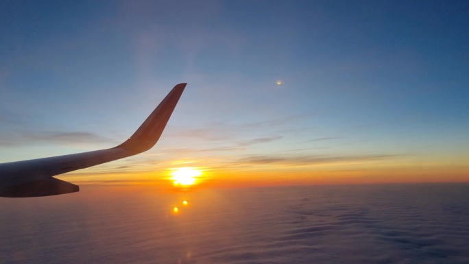 在夕阳和云彩的映衬下飞行的飞机机翼