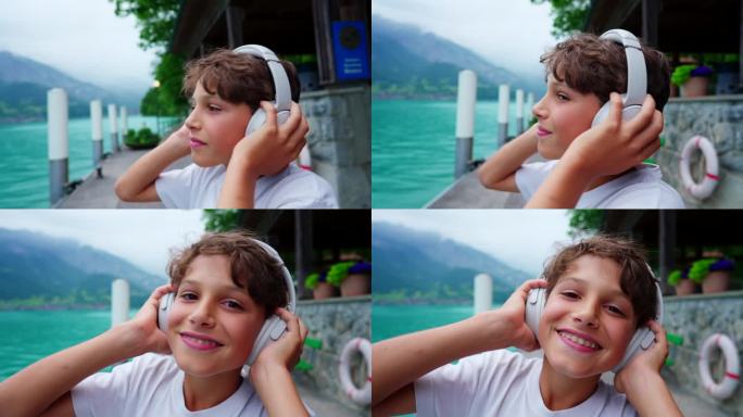 小男孩在湖边听音乐的肖像，对着镜头微笑，戴着耳机的帅孩子的特写