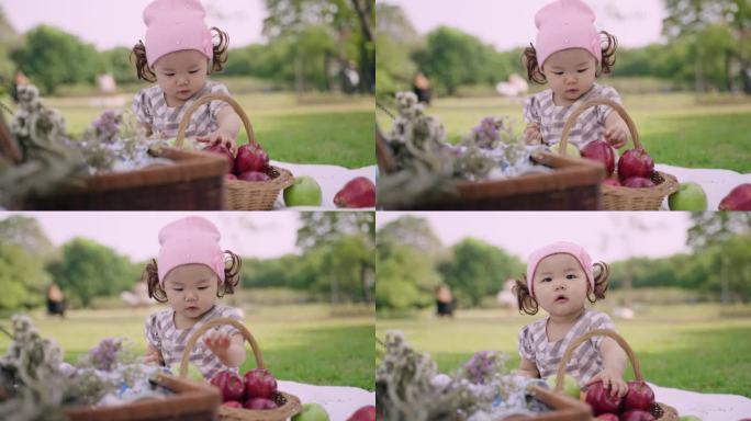 快乐可爱的小女孩坐在公园里拿着苹果，玩着苹果。