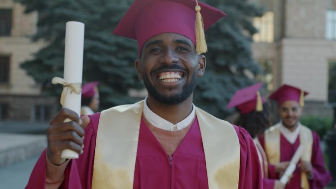 一个兴奋的非裔美国人戴着毕业帽站在校园里笑着挥舞着文凭的慢动作肖像