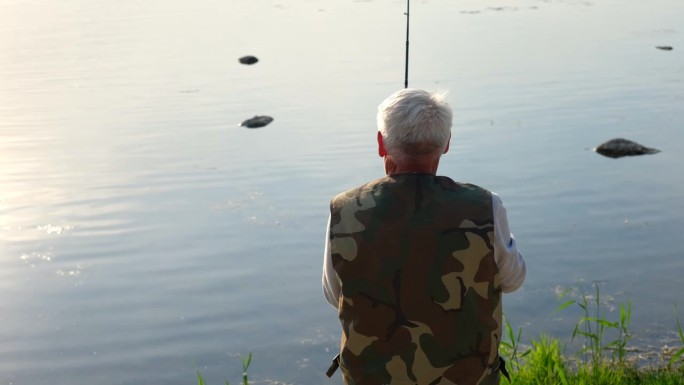老人钓鱼。夕阳西下，一位白发苍苍的老渔夫从码头上抛下一缕丝线。积极的老年男性在湖中垂钓，旋转卷轴杆。