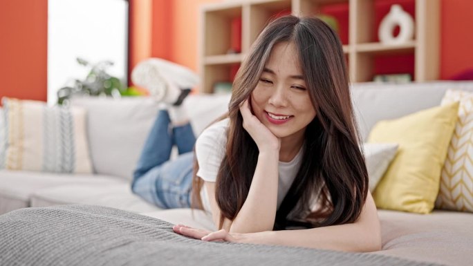 年轻的中国女人微笑地躺在家里的沙发上