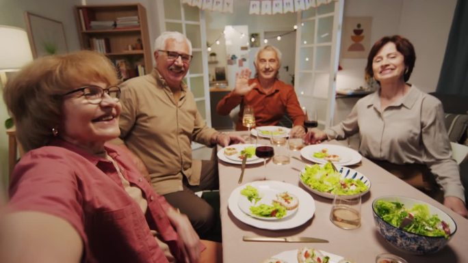 积极的老年人在餐桌上与朋友视频通话