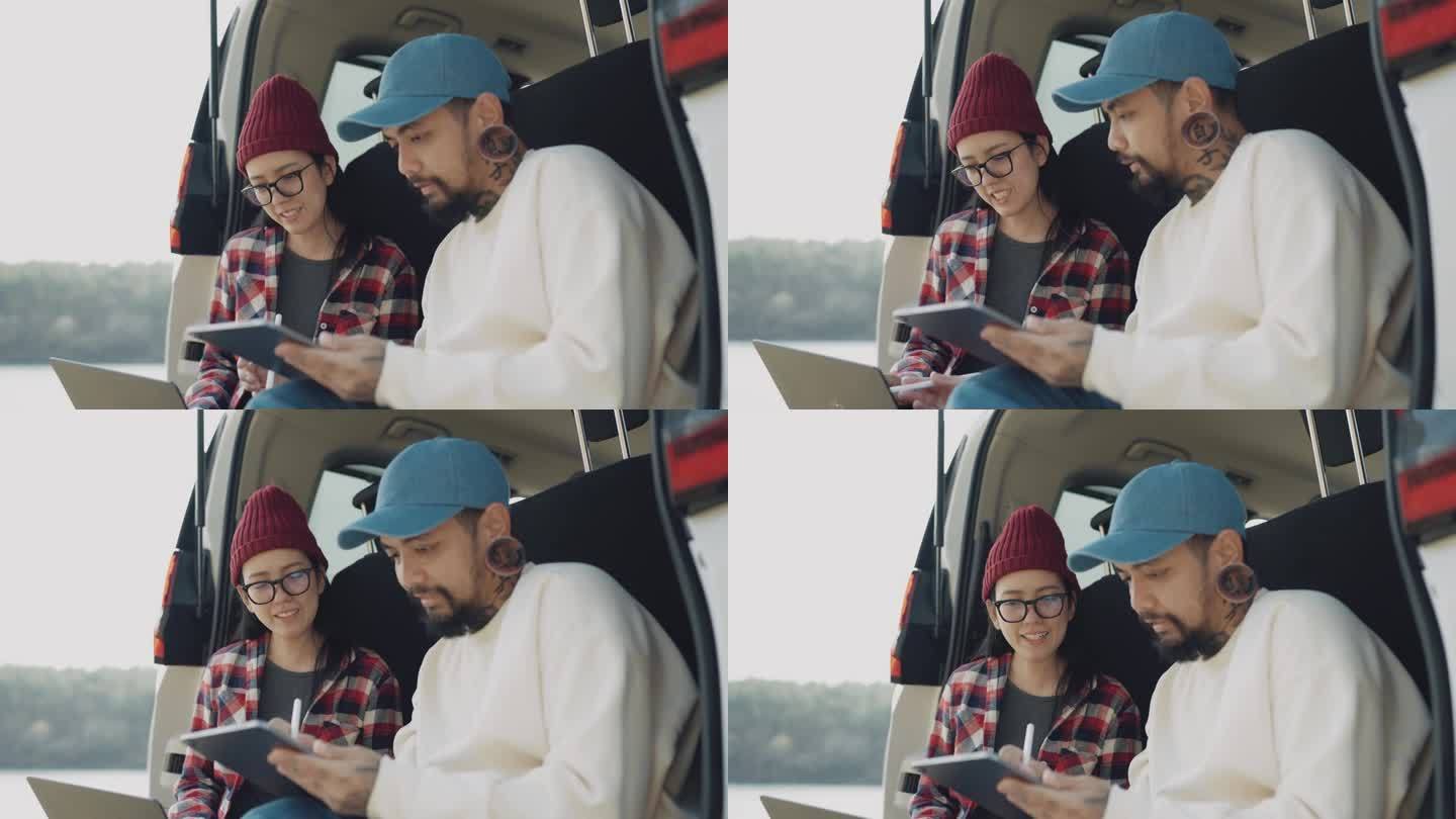 亚洲自由旅行者男女在工作日坐在汽车后备箱里聊天，使用平板电脑和笔记本电脑。