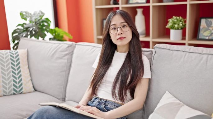 年轻的中国妇女在家里摘掉眼镜看书