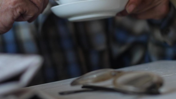 一位退休老人拿着茶托、报纸和玻璃杯，从一杯咖啡里写着早餐。老人的生活方式，爷爷看报纸新闻，喝茶