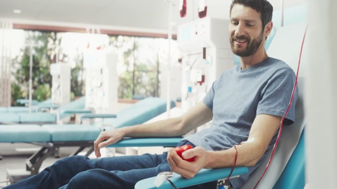 白人男子在光明医院为有需要的人献血。男性献血者挤压心形红球，将血液通过管道泵入袋中。捐赠癌症患者。