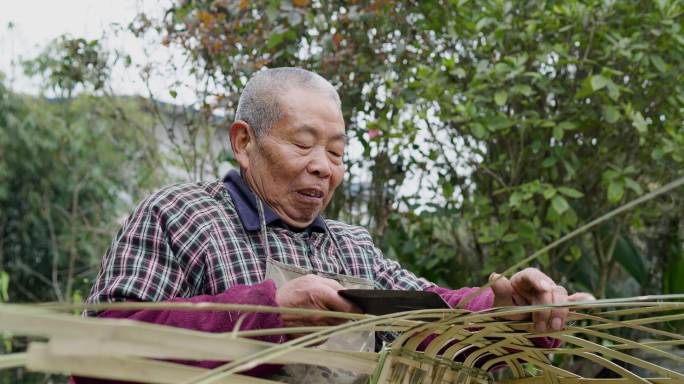 乡村老人在院子里用竹条编竹篮