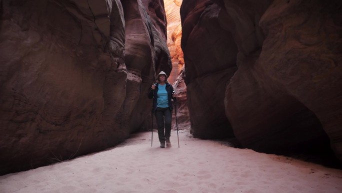 一名妇女在深槽峡谷的干涸河床上徒步旅行，那里有红橙色的弯曲岩石