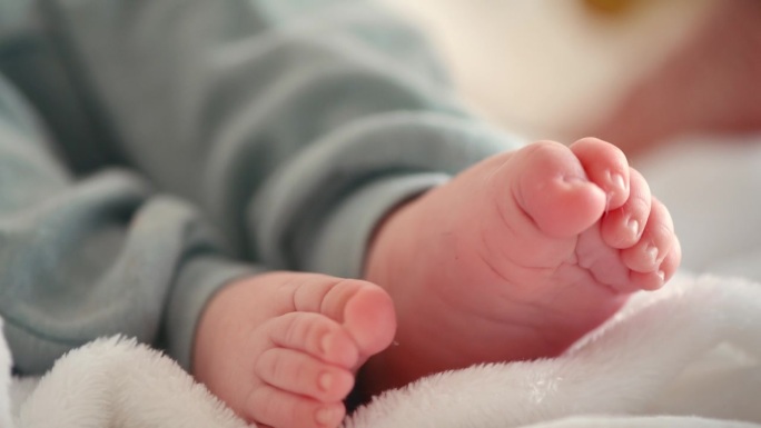 可爱，婴儿和新生儿的脚的特写躺在婴儿床上的毯子在他的家托儿所。一个小男孩在家里的卧室里放松的时候，他