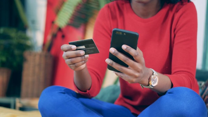 一名非洲妇女在网上购物时手持手机和卡片