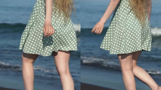 赤脚走在黑色沙滩上的女人。长腿模特身穿绿色圆点夏季连衣裙