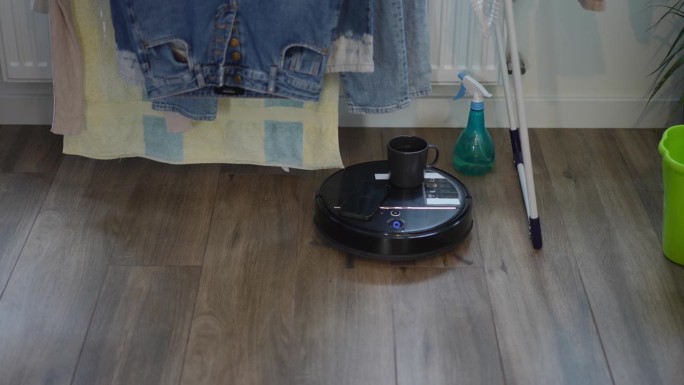 带着水杯和智能手机的扫地机器人从墙上慢动作地移动到镜头前。家用室内自动清洗机。