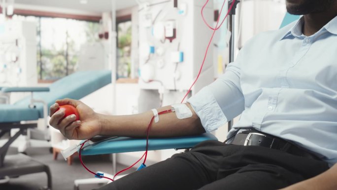 黑人男性献血者的手与连接导管的特写镜头。非洲商人挤压心形球，将血液通过管道泵入袋中。器官移植病人的捐