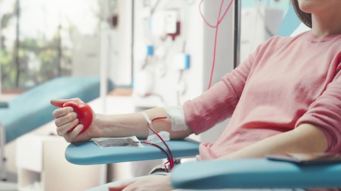 医院女献血者带导管的手部特写镜头。镜头从手掌挤压心形红球到将血液泵到白人妇女的脸上。为烧伤受害者捐款