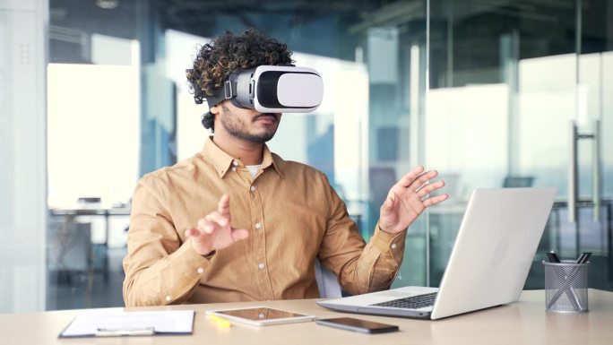 年轻成功的管理者坐在现代办公室的工作场所，在虚拟现实模拟器中使用VR眼镜工作