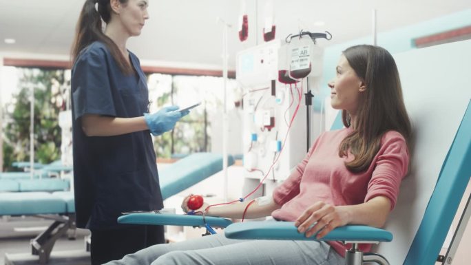 白人妇女在医院为有需要的人献血。拿着药片的女护士过来检查捐赠者的进展和健康状况。捐献给需要输血的病人