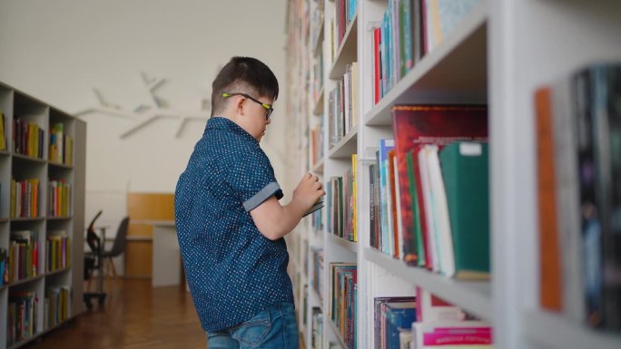 患有唐氏综合症的男孩在图书馆的书架上挑选书。社会融合