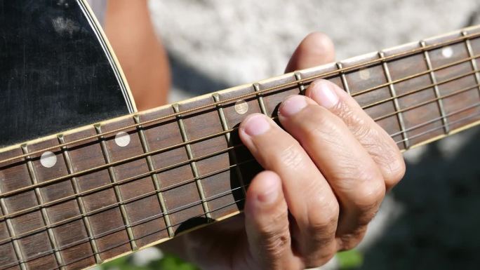 有人在户外，在阳光下弹吉他。原声吉他臂，指板前视图，特写镜头。弹原声吉他的人。在阳光下练习吉他的人。