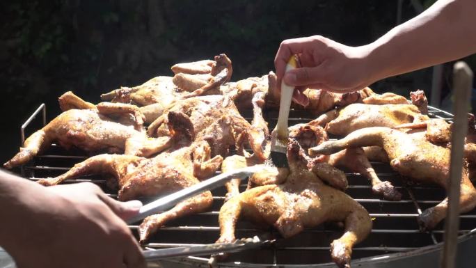 用手在木炭烧烤架上旋转烤整只腌好的鸡，加入酱汁和香草