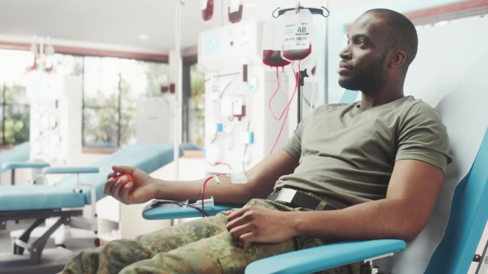 黑人男军人在军队医院为受伤战友献血。勇敢的非洲部队挤压红色心形球，将血液通过管道泵入袋中。给服役人员