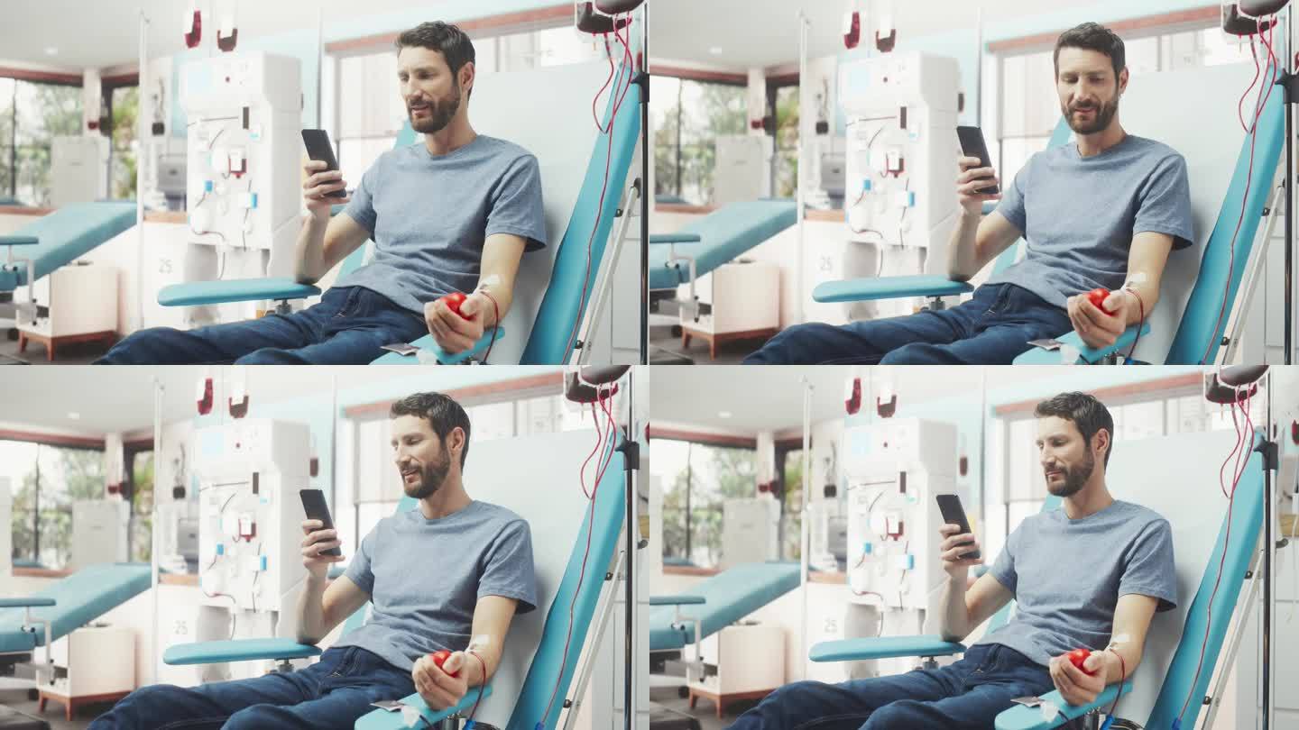 白人男子在医院为有需要的人献血。男性献血者挤压心形红球泵血，用智能手机在线聊天。器官移植病人的捐赠。