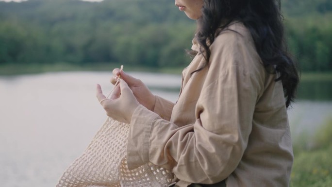 年轻女子在河边休息，在大自然中享受钩针编织。