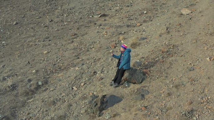 从无人机拍摄，俯视图的女人谁是坐在岩石平原上打电话。