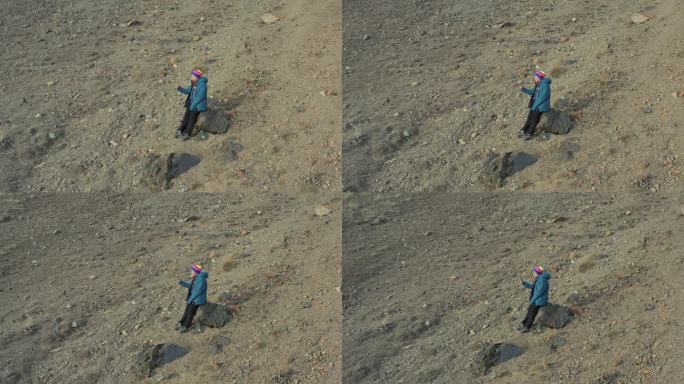 从无人机拍摄，俯视图的女人谁是坐在岩石平原上打电话。
