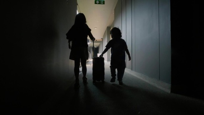 一个可爱的小女孩和她的弟弟提着一个儿童行李箱走在旅馆的走廊上。