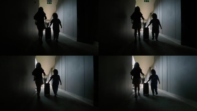 一个可爱的小女孩和她的弟弟提着一个儿童行李箱走在旅馆的走廊上。