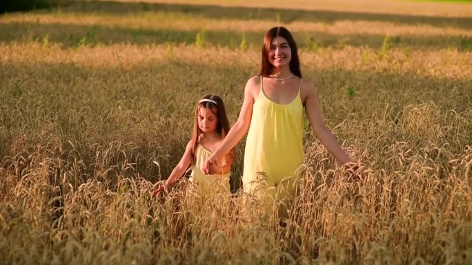 美丽的年轻妈妈和她的小女儿依偎在夕阳下的麦田里。