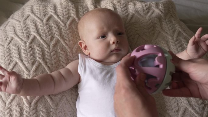 一个刚出生的小男孩躺在一个编织的蚕茧枕头上，伸开双臂看着一个玩具球。
