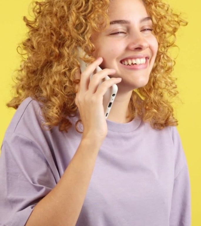 快乐的卷发女人对着手机说话