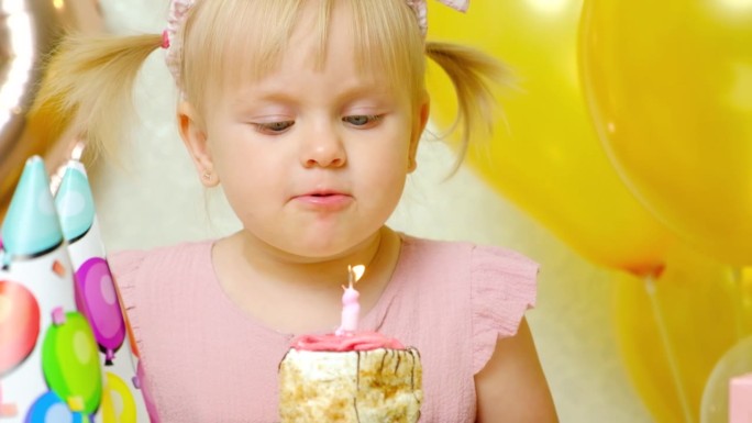 头上扎着两个马尾辫的可爱的生日女孩吹灭了生日蛋糕上的蜡烛。