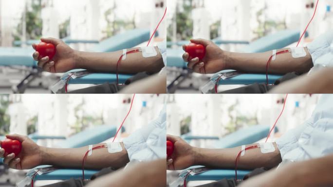 男性献血者的手的特写镜头。黑人拿着心形的红球，将血液通过管子泵进袋子。器官移植病人的捐赠。