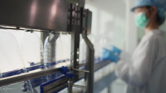 在水厂，一位穿着实验室大褂的熟练女工在装水前检查每一个塑料瓶，细致入微的质量控制世界。确保只满足最高