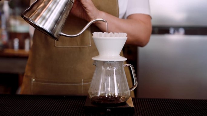 特写:咖啡师手拿水壶举起来倒咖啡粉，地址在滴漏咖啡装置中，一边喝煮好的咖啡，一边倒入热水，旋转着制作