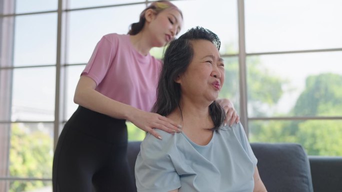 亚洲女儿给肩部按摩，帮助肩部疼痛的老母亲。小女儿在家给年迈的母亲做放松按摩。健康问题概念