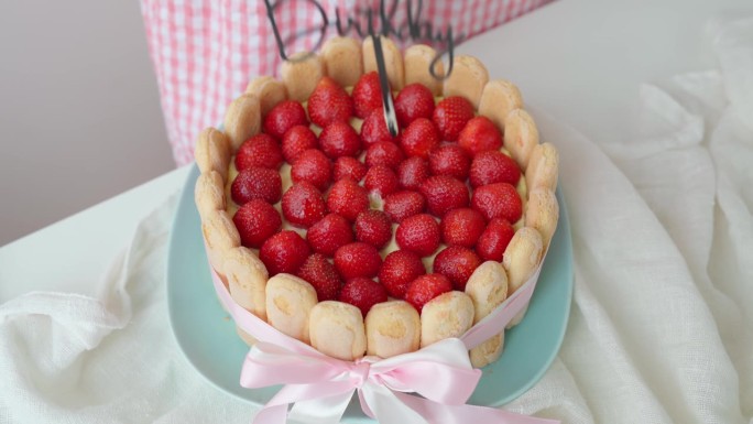 特写:女孩的手把写着“生日快乐”的横幅插进蛋糕。庆祝提拉米苏蛋糕草莓和手指饼干在一个女人面前的桌子上