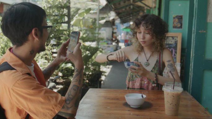 一名亚洲男子用智能手机拍下女友在餐厅享用美味泰国甜点的情景。