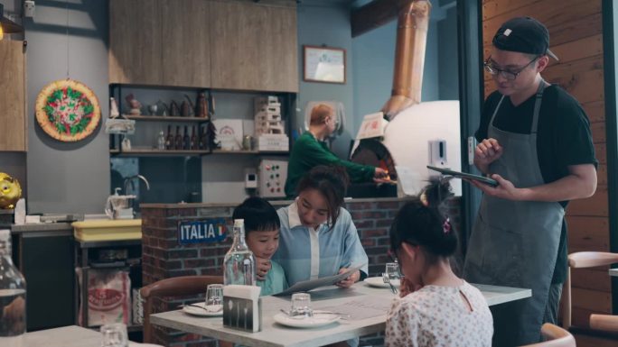图为，一位亚洲男性餐厅老板拿着平板电脑，向顾客介绍餐厅的招牌菜。他会根据顾客的喜好热情地推荐菜肴，并