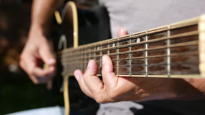 原声吉他，视野清晰。一个指板特写镜头。有人在户外弹吉他。弹原声吉他的人。在阳光下练习吉他的人。播放音