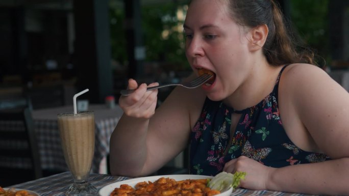 可爱胖乎乎的女孩在餐厅里吃着西红柿酱配蔬菜的大虾。